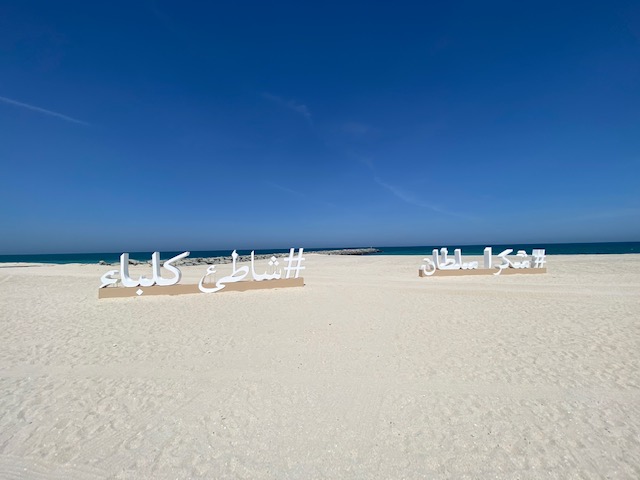 Kalba beach Sharjah, white sand with hashtag signs in Arabic and a blue sky