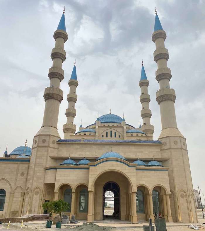 Royal Alkamali Mosque with four minarets with four balconies and blue top, and several blue domes. Under construction.