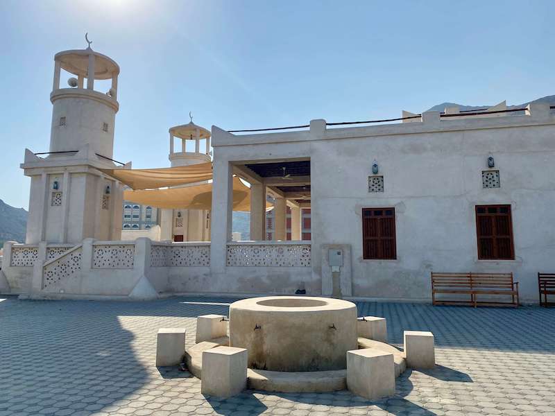 old style mosque with two wide short minarets and large stone basin for ablution outside with stone stools around it