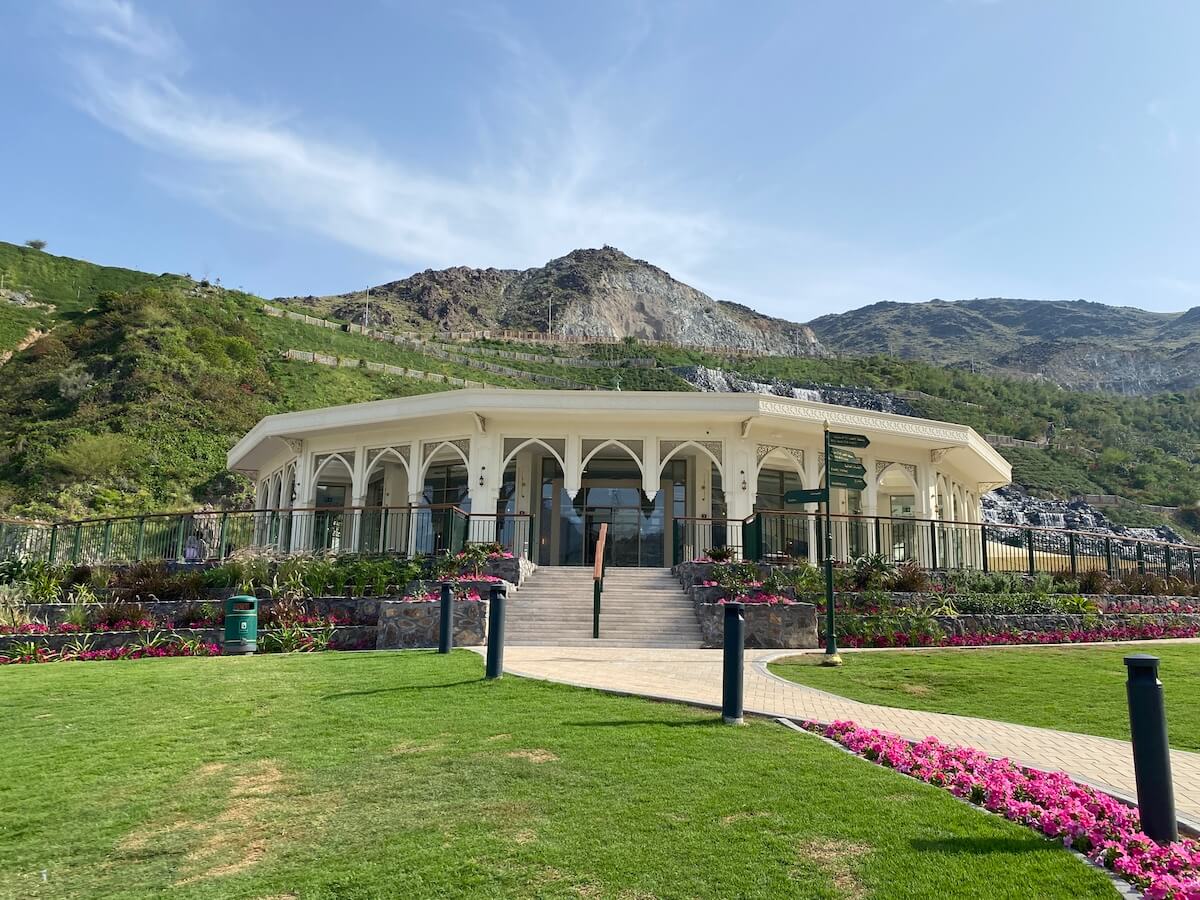 circular building with glass windows and terrace with lawn in front and mountain behind