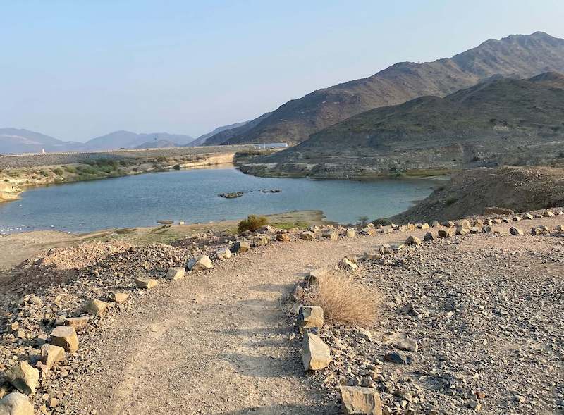 flat graded hiking trail around kalba ghail dam and lake with mountain to the right