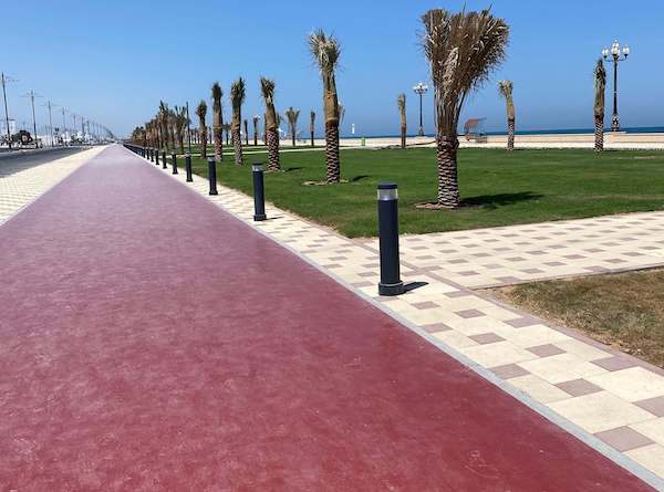 kalba walking path with beach and palm trees to the right and road to the left