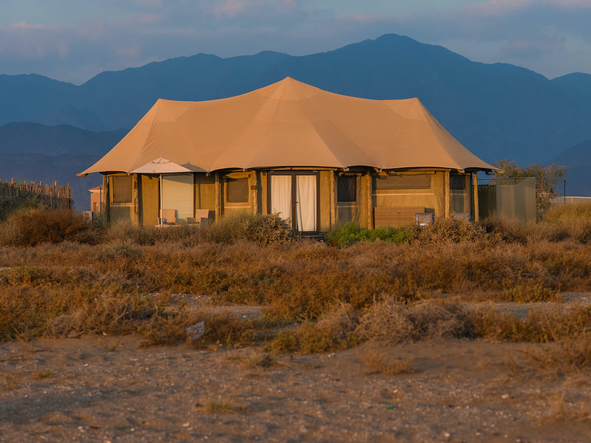 large luxury tent with brush in the foreground and mountain in the background at kingfisher retreat kalba