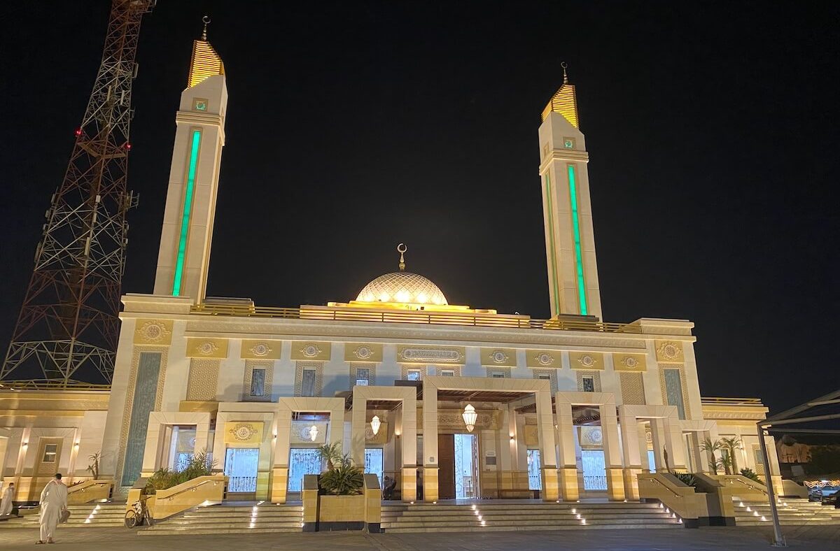 Large mosque with a dome and two minarets lit at night
