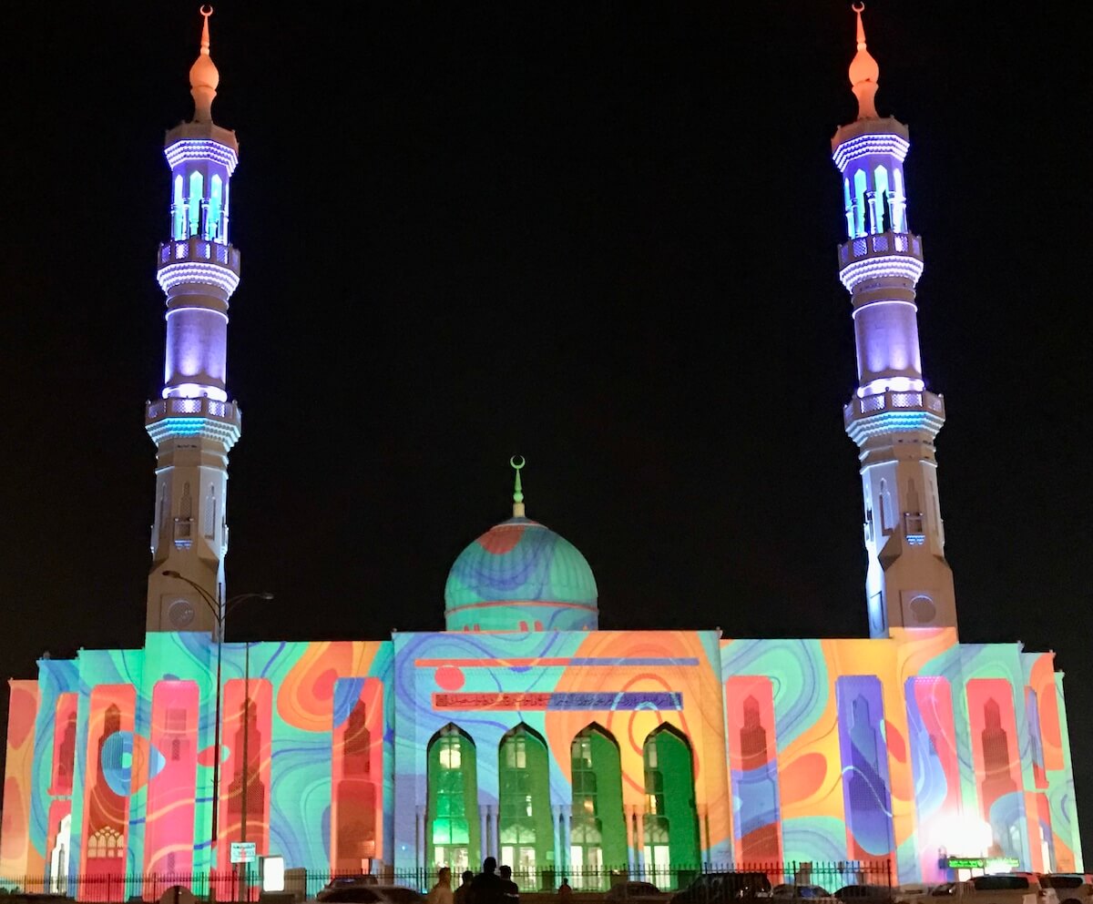 mosque with central dome and two minarets with designs projected on to it at night