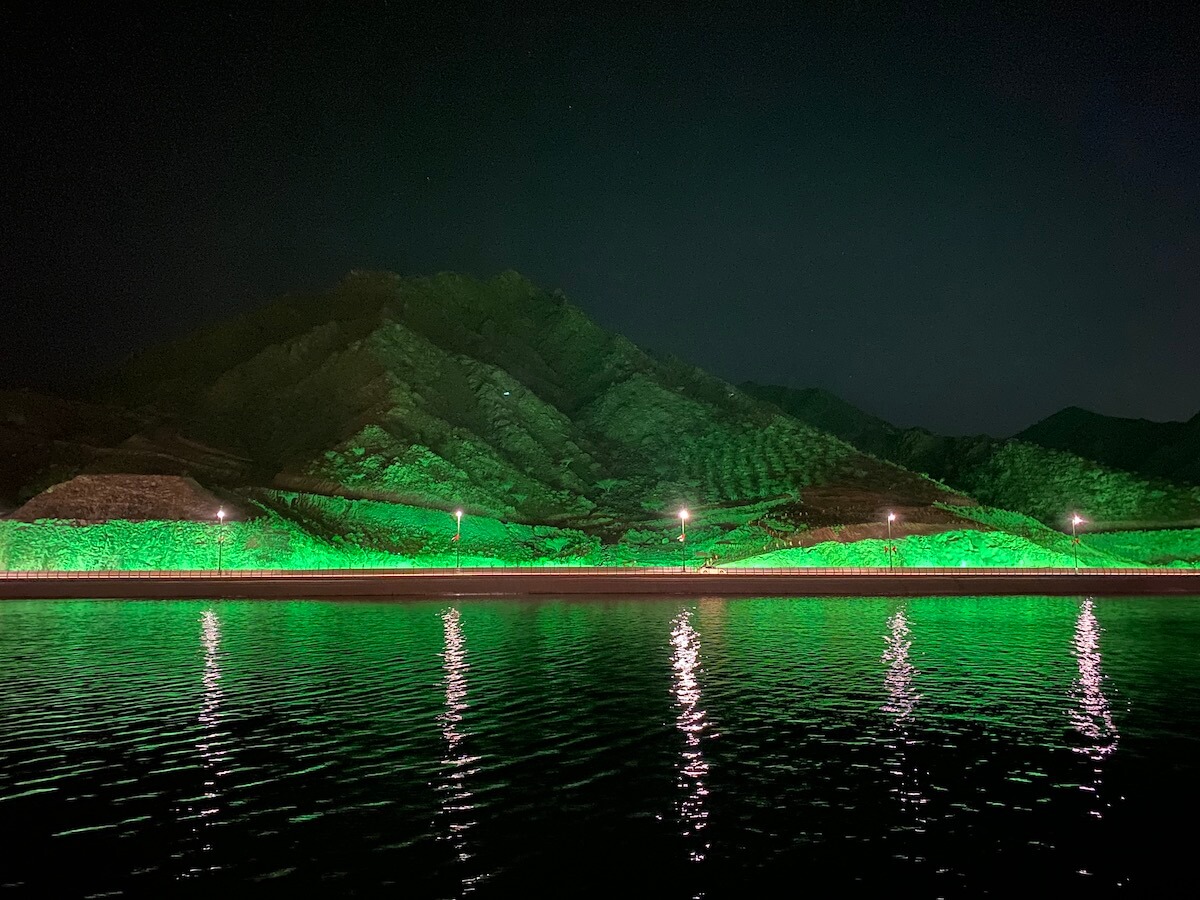 rocky mountains lit up green and reflected in lake at night