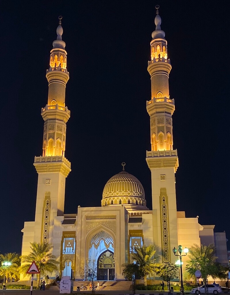 mosque with two very tall minarets and a gold dome lit up at night, black sky in background
