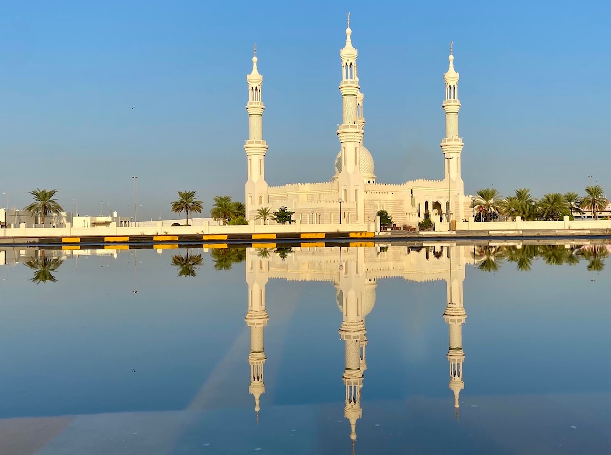 mosque with four minarets and dome 
reflected in large puddle 